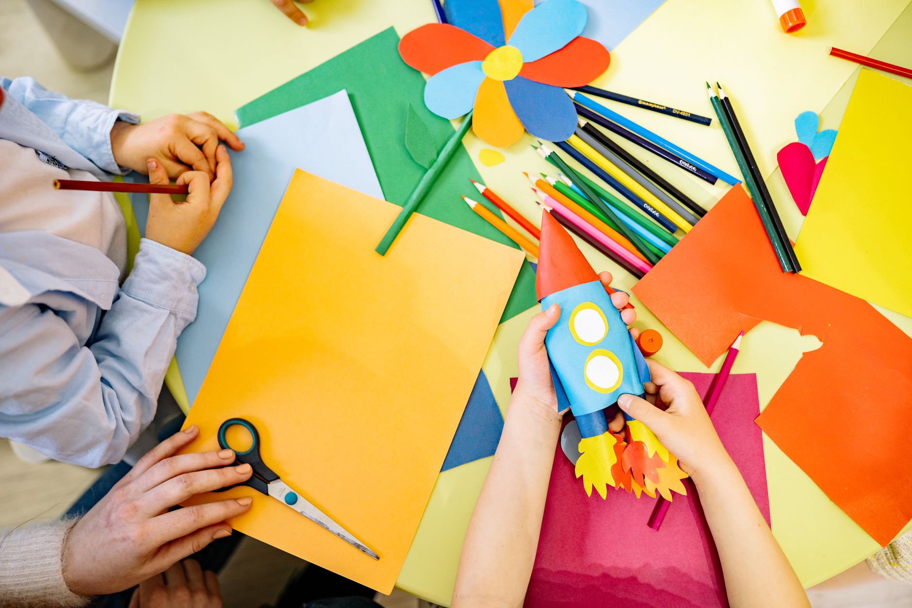 Plate 12. Scissors, pencils and a paper pinwheel on a table where two children are mid-cut.